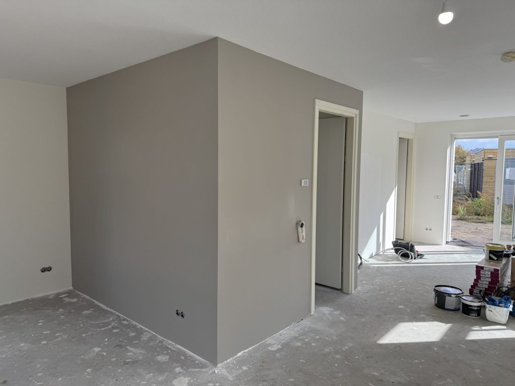 Nieuwbouwwoning met een pas geverfde grijze wand rond de meterkast, verfemmers op de betonvloer