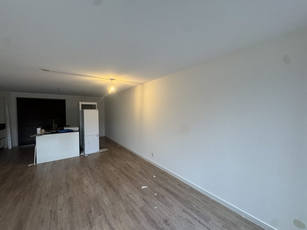 Woonkamer met een houten vloer en een lange, strak afgewerkte witte wand, de keuken nog in opbouw