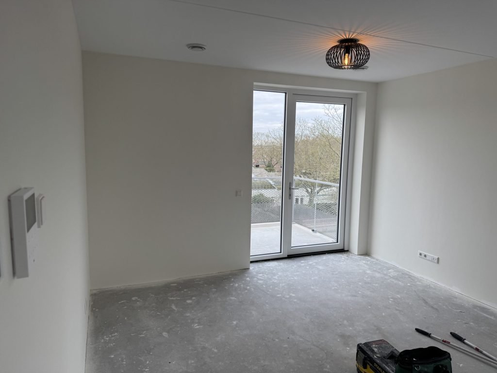 Nieuwe kamer met wit afgewerkte wanden en een balkondeur, gereedschap op de vloer